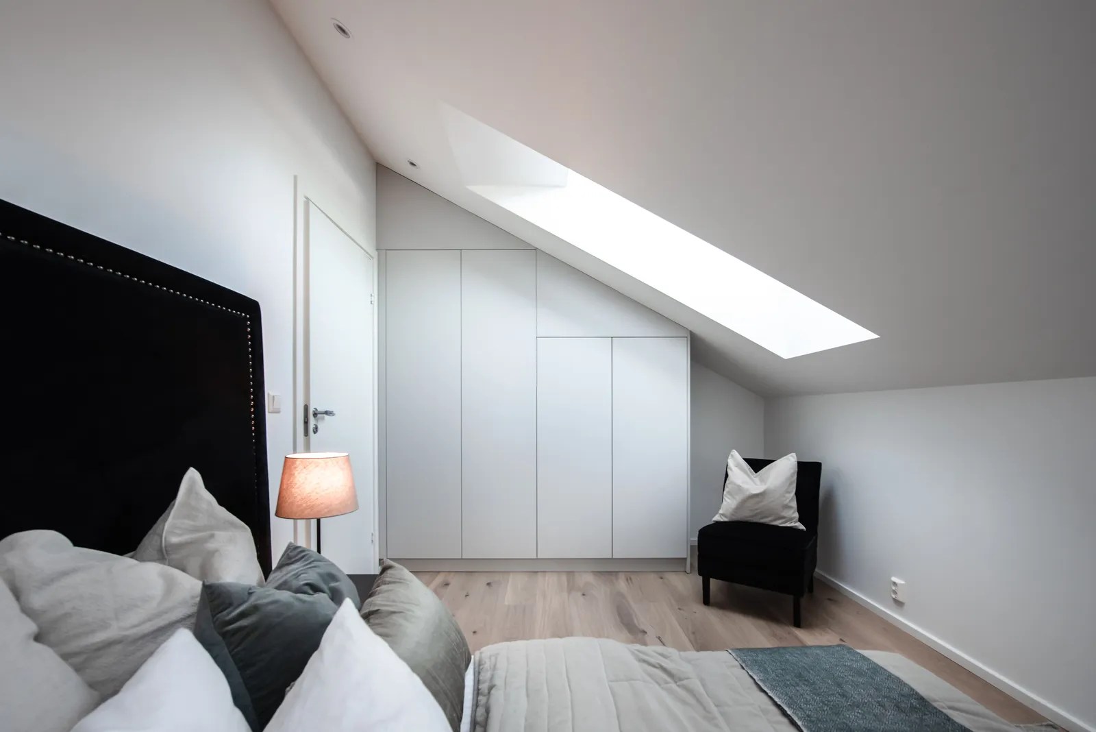 Hvit garderobe bygget inn under skråtaket på et loftsoverom med takvindu