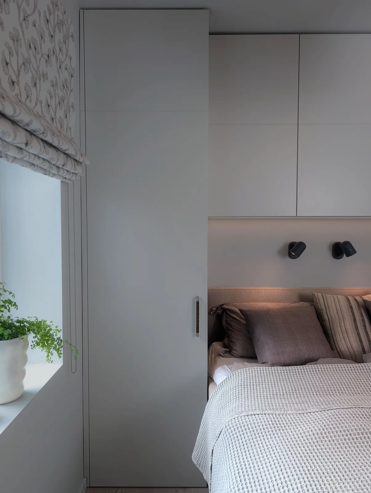 Hvit plassbygd garderobe ved siden av vinduet, sammenbygd med overskap over sengen