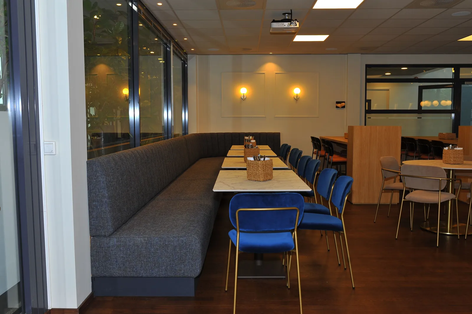 Lang sofabenk langs vinduet i en kafé med bord og blå stoler