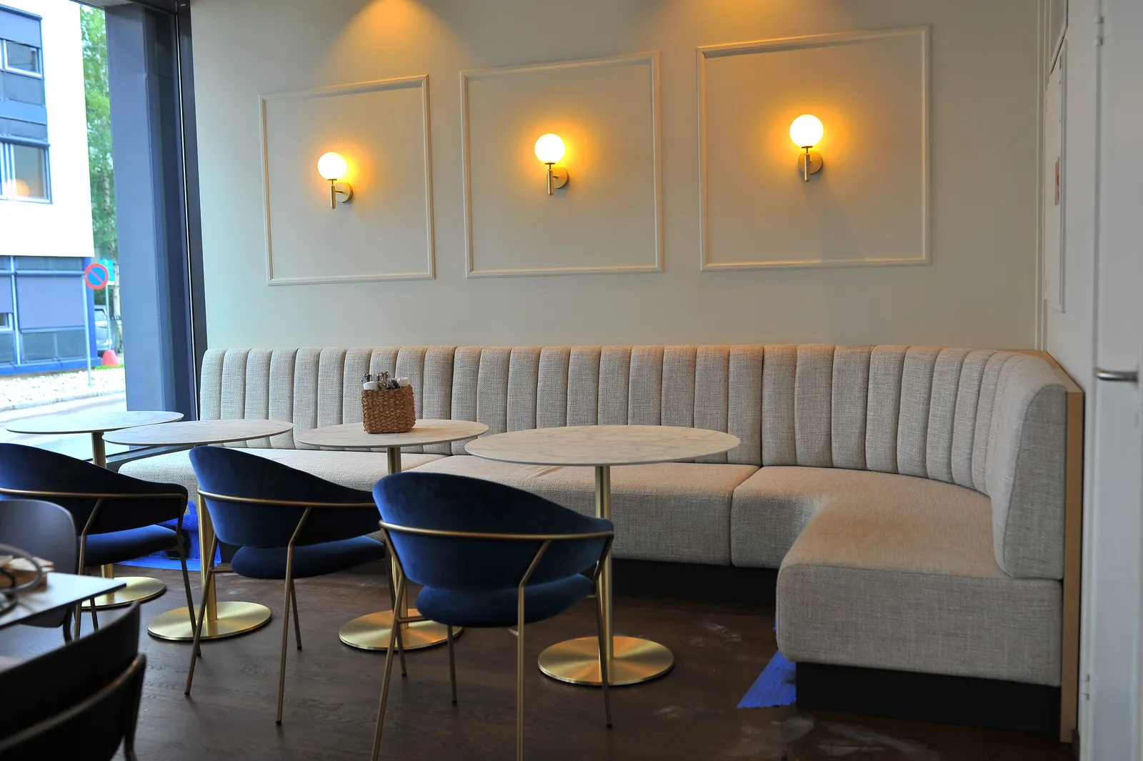 Restaurant med buet sofabenk i lyst stoff langs veggen og runde bord